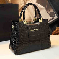 Stylish black crocodile-patterned handbag with gold accents and "Menglinkat" logo, sitting on a table against a blurred background.