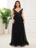 A woman in a sparkling black evening gown stands gracefully in a bright room. She smiles warmly, with lush green plants in the background. Elegant and confident tone.
