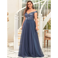 Woman in an elegant, off-the-shoulder blue gown with sequined bodice stands before a curved staircase, conveying a confident and joyful tone.