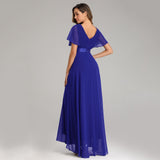 Elegant woman in a flowing blue gown with a V-back and short sleeves, standing against a neutral background, conveying grace and sophistication.
