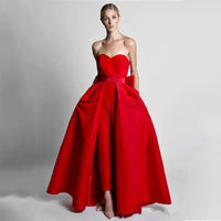 A woman wearing bright red gown with a fitted bodice, flowing overskirt, and pants underneath. The setting is a plain white background.