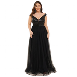 A woman wears an elegant black evening gown with sequined bodice and flowing skirt, exuding glamour and sophistication. She smiles warmly.