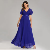 A woman in a flowing, elegant royal blue gown with short, sheer sleeves stands against a light gray background, conveying grace and elegance.