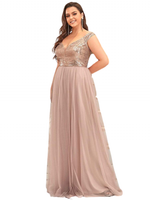 Smiling woman in a floor-length blush gown. The dress features a sparkling, fitted sequin bodice and cap sleeves, with a flowy chiffon skirt.