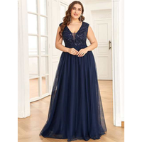 Woman in a floor-length, navy blue gown with a beaded bodice stands in a bright room with wooden floors, exuding elegance and confidence.