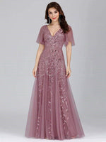 A woman wearing a flowing lavender evening gown with floral lace details. The dress features flutter sleeves and a V-neck, conveying elegance and grace.