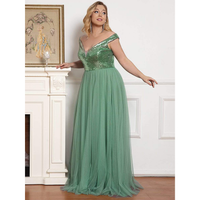 A smiling woman in a green, off-the-shoulder gown stands beside a white fireplace. A framed floral artwork and a glass are on the mantel.