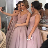 Three women in matching blush pink dresses take a selfie. They stand close together, smiling, in a warmly lit room, projecting joy and friendship.