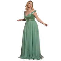 Woman in an elegant, off-shoulder green gown with a sequined bodice and flowing tulle skirt. She appears poised, evoking a sense of grace.
