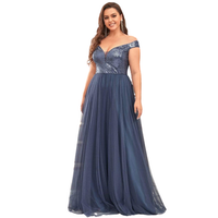 A woman in an elegant, off-shoulder navy blue gown with a shimmering top and flowing tulle skirt. She smiles, exuding confidence and grace.