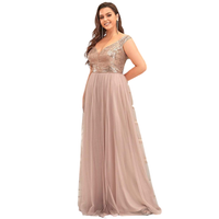 Woman in a floor-length, sleeveless gown with a sequined bodice and flowing pink skirt, smiling with hands on hips. Elegant and confident tone.