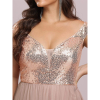A woman in a sequined rose gold dress with a deep V-neckline poses with her hand on her hip. She wears long, dangling earrings, exuding elegance.
