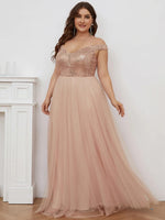 A woman in a shimmering peach gown with off-shoulder straps stands gracefully by a white mantel. Her expression is joyful, conveying elegance.