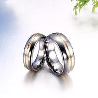 Two intertwined silver rings with gold accents rest on a smooth, reflective surface. The light creates a sleek, elegant appearance with a romantic tone.