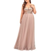 A woman in a flowing, sleeveless blush gown with a sequin bodice and V-neckline stands elegantly, hand placed on chest, conveying grace.