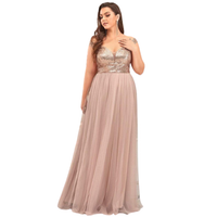A woman in an elegant, sleeveless evening gown with a sequined bodice and flowing pink skirt. She exudes confidence, touching her chest gently.
